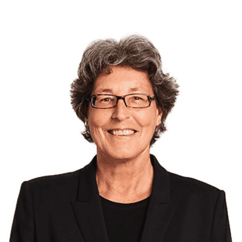 Smiling Guest Speaker Marcia Hyde with short, grey, curly hair, wearing glasses and a black blazer, stands against a plain white background.