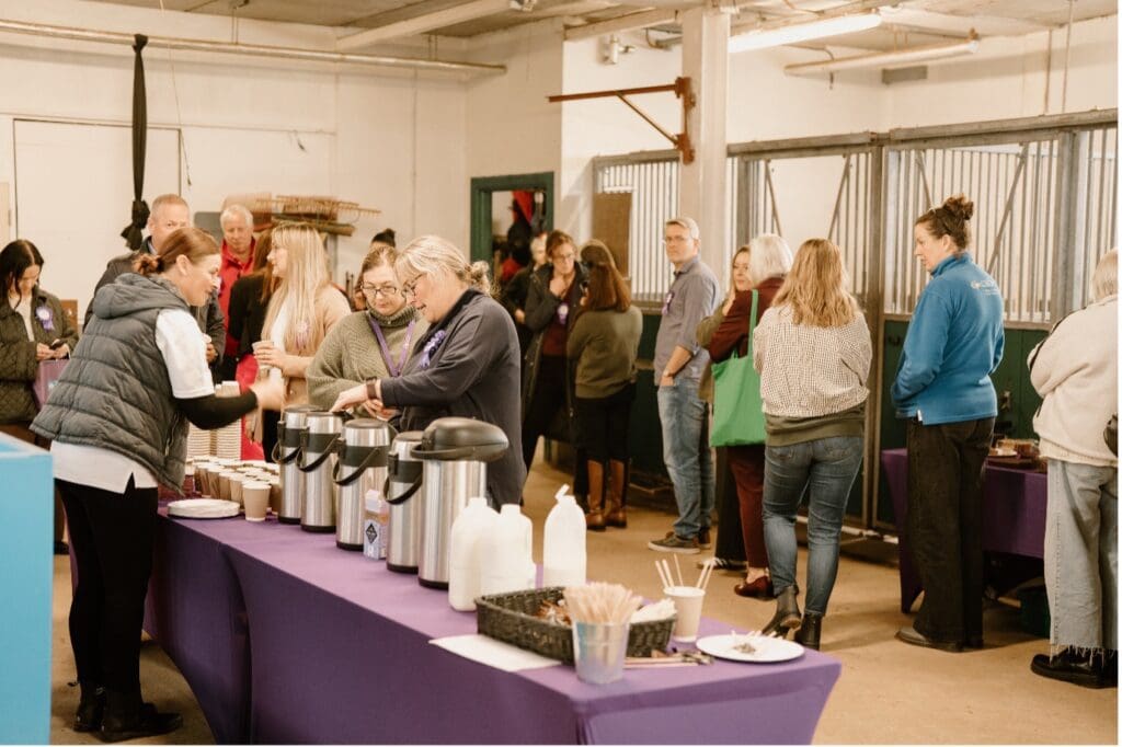 People are gathered indoors, standing in a queue by tables with coffee dispensers, cups, and condiments. The casual, social atmosphere reflects Causeway Coast & Glens RDA: The Link – Connecting Cruelty’s welcoming spirit.
